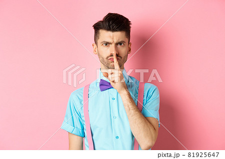 Angry and grumpy man in funny bow-tie shushing at camera, frowning and demand silence, tell to be quiet, scolding someone loud, standing on pink background Angry and grumpy man in funny bow-tie shushing at camera, frowning and demand silence, tell to be quiet, scolding someone loud, standing on pink background 81925647