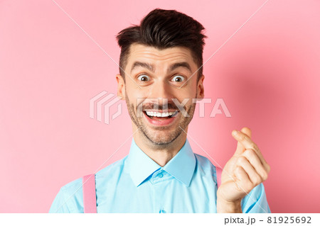 Valentines day concept. Smiling man showing finger heart and looking happy, standing over pink background 81925692