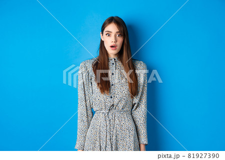 Shocked cute girl in dress looking at camera with opened mouth, gasping startled, see something shocking, standing on blue background Shocked cute girl in dress looking at camera with opened mouth, gasping startled, see something shocking, standing on blue background 81927390