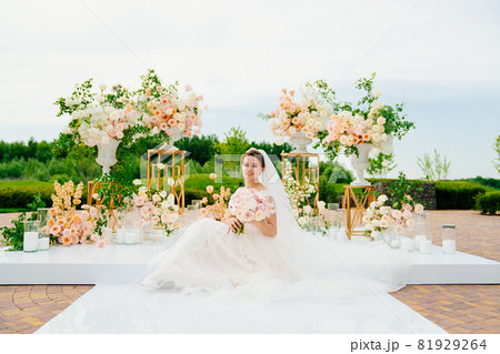 bride in the wedding ceremony area of live white and pink flowers.  81929264