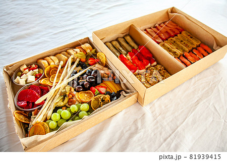 Delicious wine snacks in a cardboard box for a buffet for a party: cheeses, sausages, cold cuts, fruit, baguette, Grissini 81939415