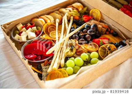 Delicious wine snacks in a cardboard box for a buffet for a party: cheeses, sausages, cold cuts, fruit, baguette, Grissini Delicious wine snacks in a cardboard box for a buffet for a party: cheeses, sausages, cold cuts, fruit, baguette, Grissini 81939416