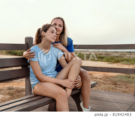 Mother and daughter sitting on a bench together at sunset 81942463