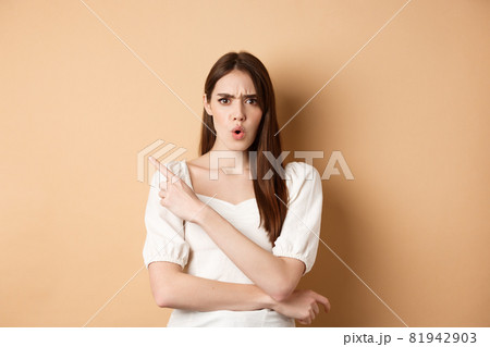What is that. Shocked and angry woman scolding person, frowning and pointing left with confused face, waiting for explanation, standing on beige background 81942903
