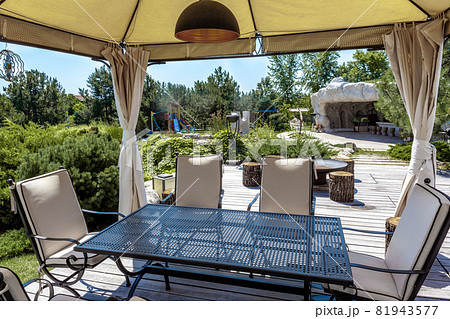 Patio with dining table in garden tent and BBQ area in backyard of country mansion 81943577
