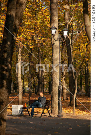 Sad man is sitting on a bench in an autumn city park with a bouquet of flowers and waits for a long time with a dissatisfied expression on his face. A failed date 81943895