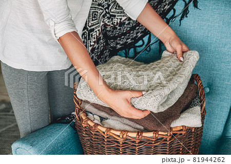 Women's hands fold a stack of warm knitted sweaters in wicker b 81944262