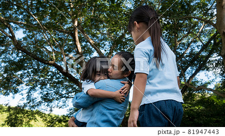 Two sibling little girls with mom laughing and hugging each other on warm and sunny summer day in the garden. Young girls with her mother spending day in park. Two sibling little girls with mom laughing and hugging each other on warm and sunny summer day in the garden. Young girls with her mother spending day in park. 81947443