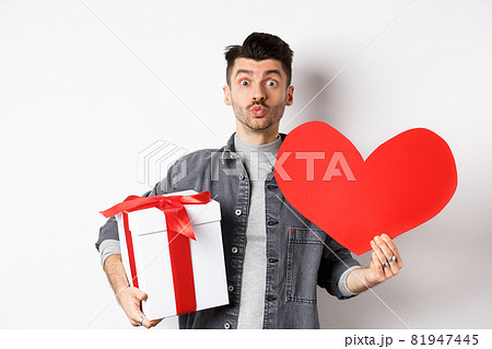 Valentines day and love concept. Guy waiting for kiss, bring lovely gifts and red heart card, pucker lips and look at camera, celebrating romantic holiday Valentines day and love concept. Guy waiting for kiss, bring lovely gifts and red heart card, pucker lips and look at camera, celebrating romantic holiday 81947445