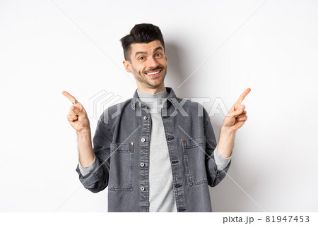 Young handsome guy with moustache pointing fingers sideways, showing two logos, smiling happy at camera, standing in casual clothes on white background Young handsome guy with moustache pointing fingers sideways, showing two logos, smiling happy at camera, standing in casual clothes on white background 81947453
