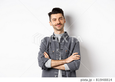 Proud handsome guy looking satisfied, cross arms on chest and smile at camera, checking out something good, standing on white background 81948814