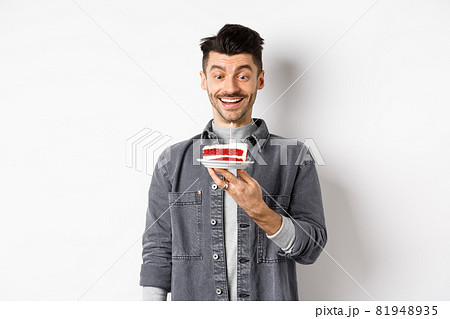 Happy birthday guy making wish on b-day cake, smiling and looking at lit candle excited, standing on white background 81948935