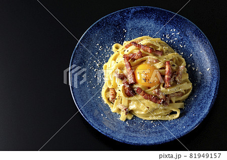 卵黄やカリカリに焼いたベーコンが入っているフェットチーネのカルボナーラを黒背景で俯瞰撮影 81949157