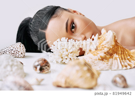Fashion portrait of beautiful african american woman with different seashells looking through conch 81949642