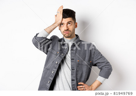Annoyed young man looking tired or bothered, roll eyes and slap forehead, making facepalm from something stupid, standing on white background 81949769
