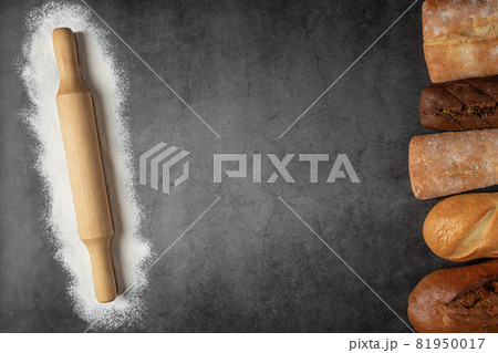 Baking dark background with copy space with various fresh baked bread and rolling pin with ingredient flour top view. 81950017