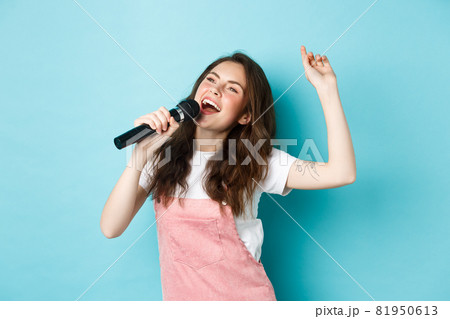 Happy young woman perform song, singer holding microphone, dancing and singing at karaoke, standing over blue background Happy young woman perform song, singer holding microphone, dancing and singing at karaoke, standing over blue background 81950613