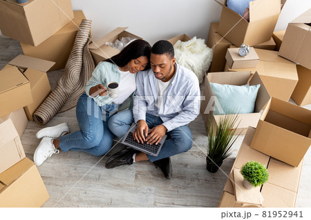 Moving, relocating concept. Loving african american couple purchasing furniture for new apartment, using laptop Moving, relocating concept. Loving african american couple purchasing furniture for new apartment, using laptop 81952941