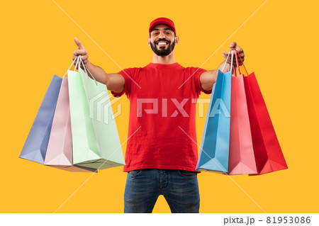 Middle-Eastern Male Courier Giving Shopper Bags Delivering Clothes, Yellow Background 81953086
