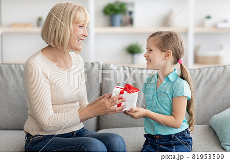 Little girl greeting mature lady giving box 81953599