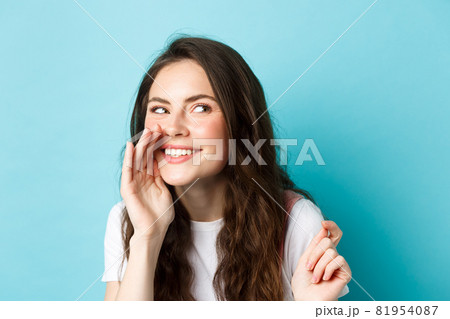 Cunning silly woman spread gossips, talking quiet, telling rumour, smiling and giggle at right side, standing over blue background Cunning silly woman spread gossips, talking quiet, telling rumour, smiling and giggle at right side, standing over blue background 81954087