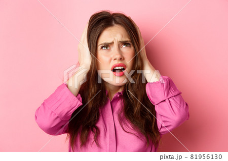 Close up of annoyed glamour girl covering ears with hands, looking bothered up at neighbours, cant stand loud music, standing over pink background 81956130