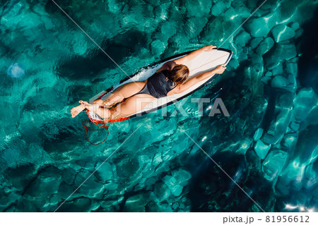 Surf girl on surfboard in transparent turquoise ocean. Aerial view with surfer woman Surf girl on surfboard in transparent turquoise ocean. Aerial view with surfer woman 81956612