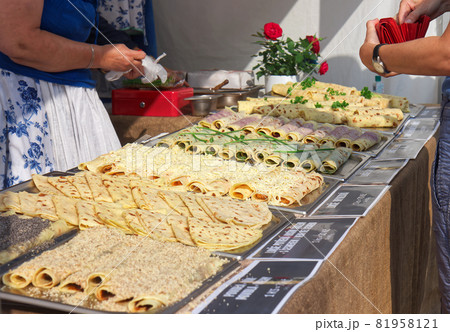 A market stall with sweet and savoury potato pancakes called "lokse". A customer buys food at a stall selling potato pancakes. Focus on the pancakes with grated cheese and the customer with his wallet 81958121