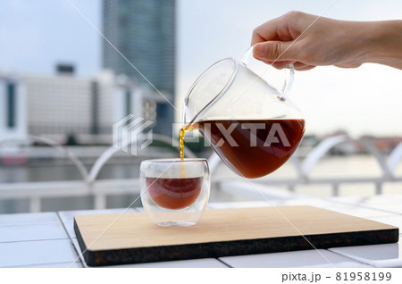 Close up pouring hot black coffee from the coffee pot into a cup on the balcony by the river. Copy space. 81958199