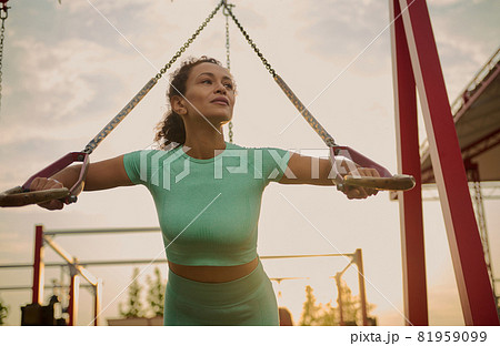Powerful attractive muscular African American woman fitness trainer do battle workout with ropes, suspension straps in the outdoor sportsground at sunrise. Healthy lifestyle, fitness and sport concept Powerful attractive muscular African American woman fitness trainer do battle workout with ropes, suspension straps in the outdoor sportsground at sunrise. Healthy lifestyle, fitness and sport concept 81959099