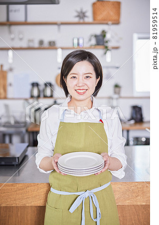 キッチンでお皿を持って立つエプロン姿の若い女性 キッチンでお皿を持って立つエプロン姿の若い女性 81959514