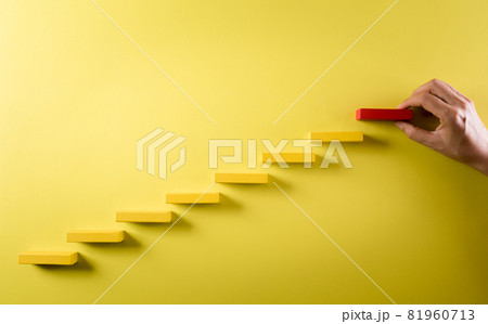 Concept of building success foundation. Hand holding wooden block stacking as step stair, Success in business growth concept on yellow background. Concept of building success foundation. Hand holding wooden block stacking as step stair, Success in business growth concept on yellow background. 81960713