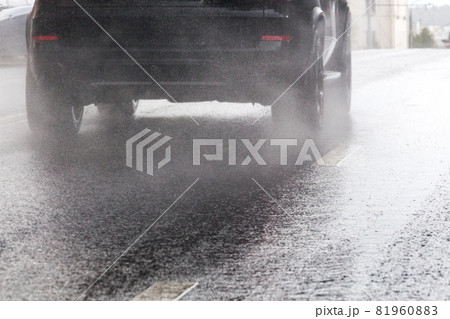 rain water splash flow from wheels of black car moving fast in daylight city with selective focus 81960883