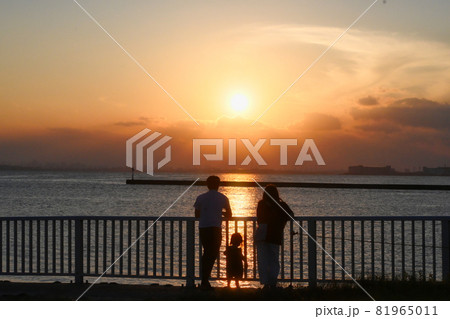 海岸で夕日を見ている親子の後ろ姿のシルエットの写真素材