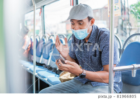 Happy asian man cheering celebrating looking at smartphone while in public bus with mask 81966805