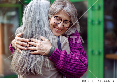 Smiling mature woman embraces female friend meeting on modern city street Smiling mature woman embraces female friend meeting on modern city street 81966813