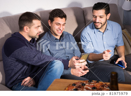 Cheerful men using phone while enjoying beer at home Cheerful men using phone while enjoying beer at home 81975979