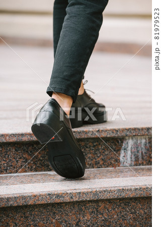 Close-up photo of young woman in black fur coat, jeanse and shoes posing on stairs Close-up photo of young woman in black fur coat, jeanse and shoes posing on stairs 81979523