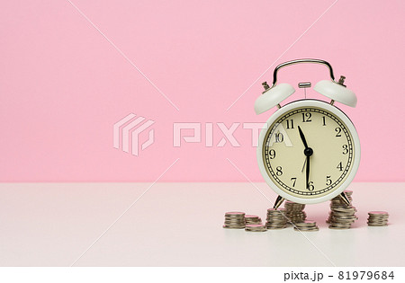 stack of coins round white alarm clock on the table. The concept of time is money, a period of discounts. stack of coins round white alarm clock on the table. The concept of time is money, a period of discounts. 81979684