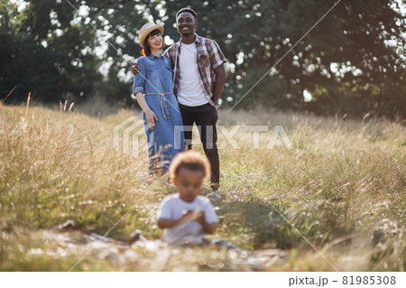 Mixed race parents looking at son that playing in grass 81985308
