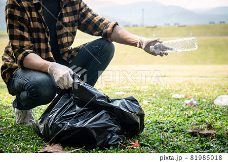 Volunteer man in gloves sitting to picking up plastic bottle into plastic black bag for cleaning the park 81986018