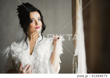 Gorgeous bride in robe posing and preparing for the wedding ceremony face in a room Gorgeous bride in robe posing and preparing for the wedding ceremony face in a room 81988679