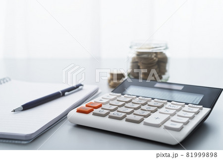 電卓とビンに貯めた貨幣。家計の管理とお金の節約。 81999898