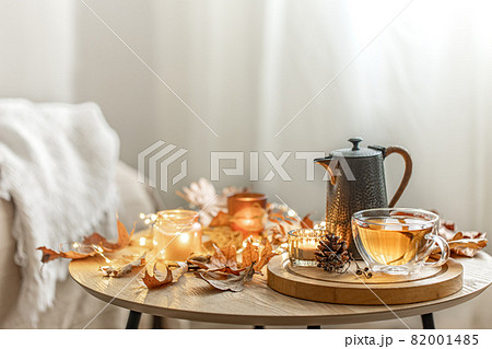 Cozy composition with a cup of tea, a teapot, candles and autumn leaves. 82001485