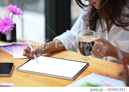 Cropped shot young woman holding coffee cup and working with digital tablet in creative office. 82002301