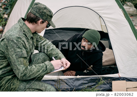 Soldier in army uniform crouching at tent of black man while performing count of migrants Soldier in army uniform crouching at tent of black man while performing count of migrants 82003062