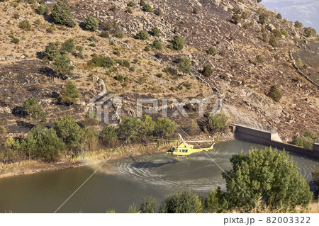 Firefighting helicopter taking water from a dam to extinguish a forest fire. Hazard concept Firefighting helicopter taking water from a dam to extinguish a forest fire. Hazard concept 82003322