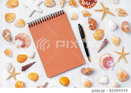Open notepad with sea shells on white wooden background 82004544