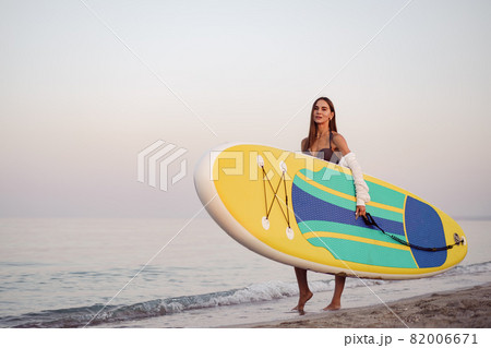 Young woman is carrying paddle board at the beach 82006671