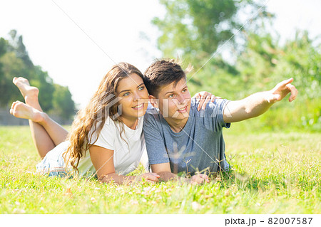 Happy couple lie on grass point with hand to something Happy couple lie on grass point with hand to something 82007587